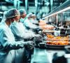 Arbeiter in Schutzkleidung während der Produktion von Lebensmitteln an einem Tisch