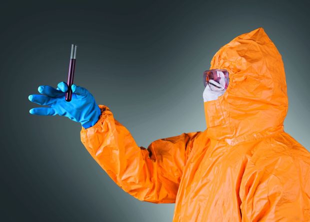 Mensch in Schutzkleidung hält Reagenzglas mit Blut darin